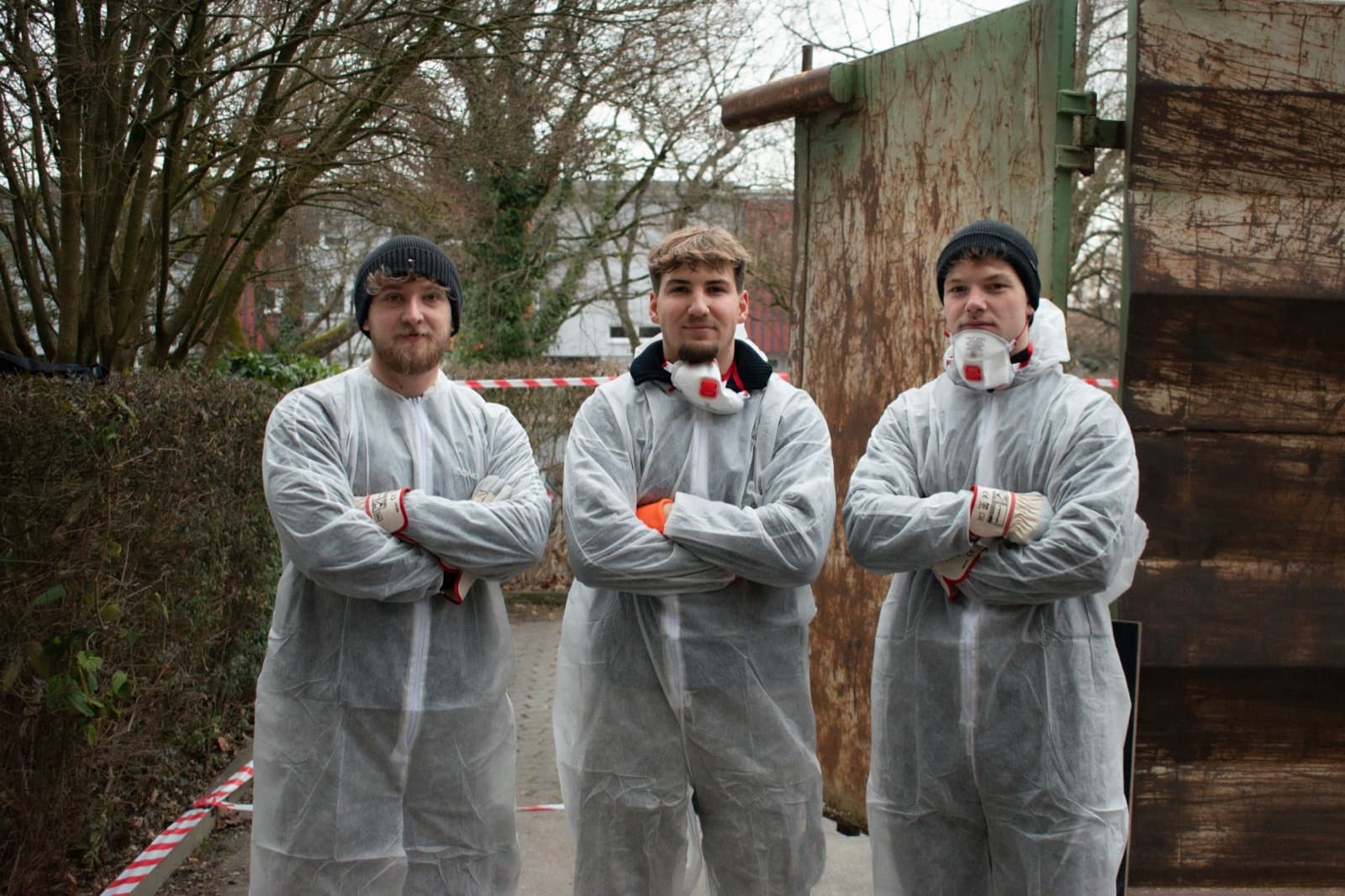 Das Heimathelfer-Team in Schutzkleidung vor einem Entsorgungscontainer