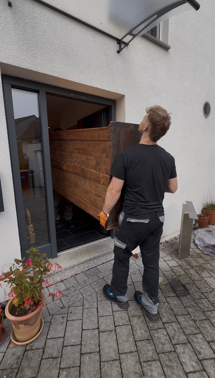 Heimathelfer-Mitarbeiter trägt eine schwere Kiste in ein Haus